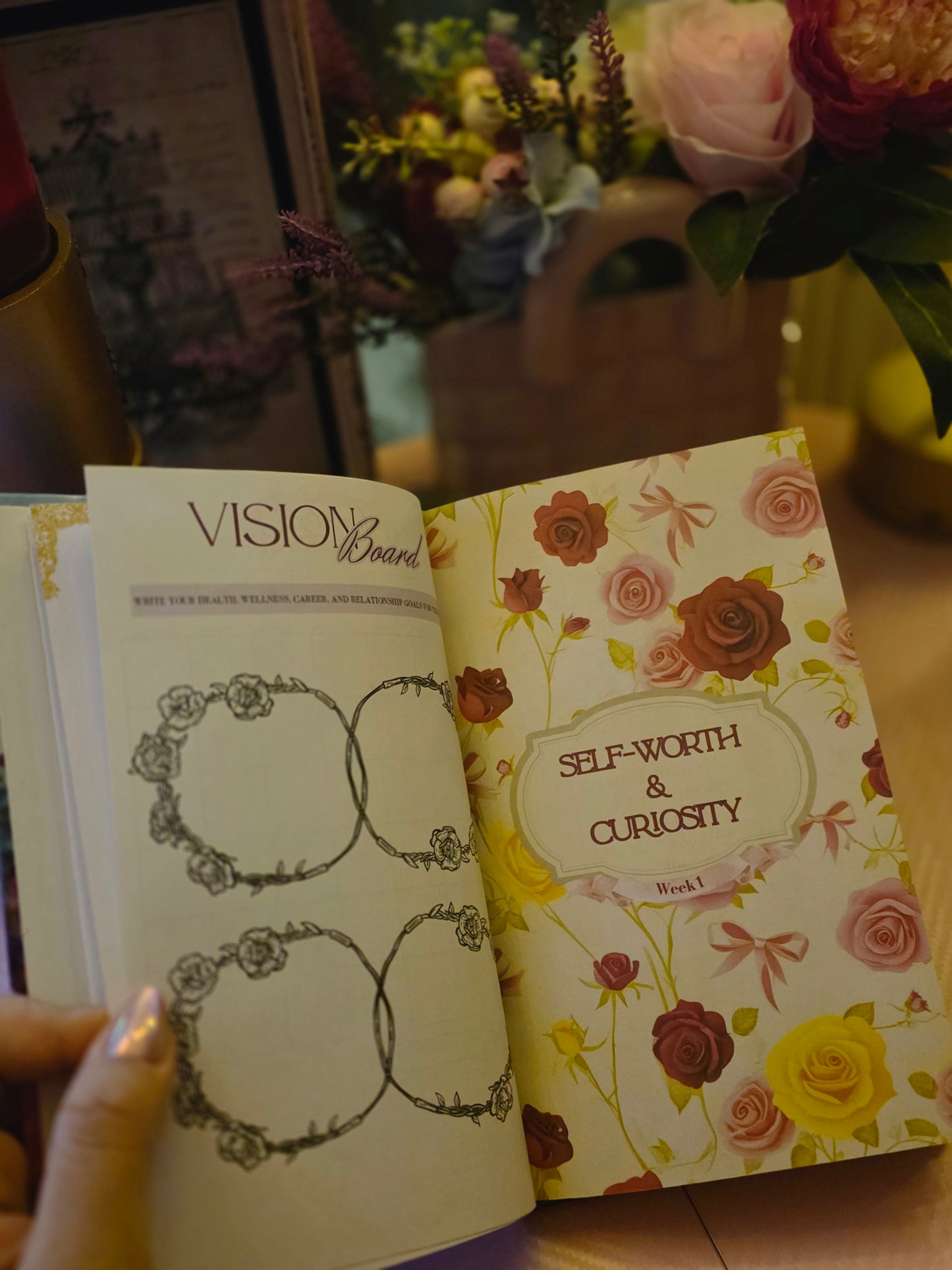 Open book with floral design on the cover, held by a hand with a blurred background of flowers.