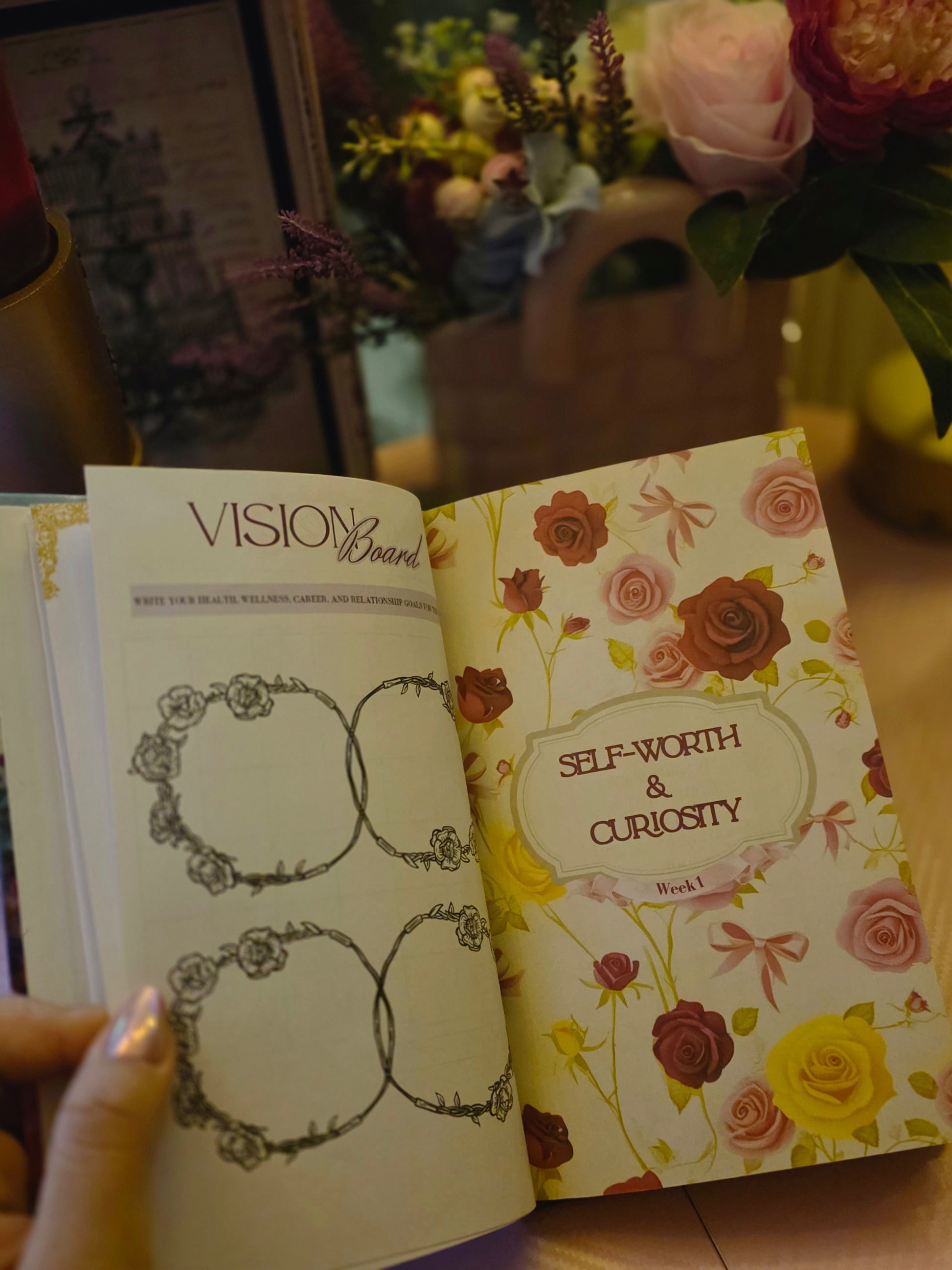 Open book with floral design on the cover, held by a hand with a blurred background of flowers.